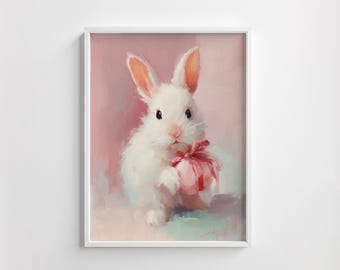 Op de afbeelding: Een ingelijst schilderij van een wit konijn met een roze cadeau met een roze strik. Het konijn heeft lange oren en zwarte ogen. De achtergrond is zachtroze en lichtblauw.