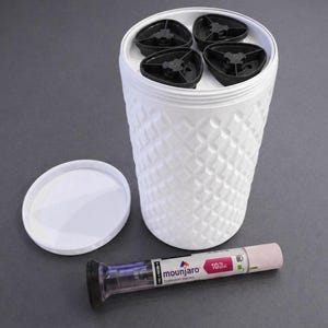 Puede incluir: Contenedor blanco texturizado con tapa, que contiene cuatro objetos triangulares negros. Un bolígrafo de inyección Mounjaro está al lado del contenedor. El bolígrafo es rosa y transparente con el texto "Mounjaro" y "10".