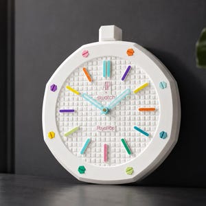 May include: A white wall clock with an octagonal frame and a textured grid dial. The clock features colourful hour markers, light blue hands, and the text AP, swatch, and Royal Oak printed on the face. The design includes small screw-like accents.