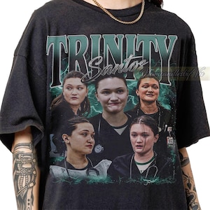 Könnte beinhalten: Ein schwarzes Kurzarm-T-Shirt mit einem Grafikdruck, der den Text TRINITY und Santos in einer stilisierten Schriftart zeigt. Das Design enthält fünf fotografische Porträts derselben Person in medizinischer Kleidung mit Stethoskop vor einem grünen Blitzhintergrund.