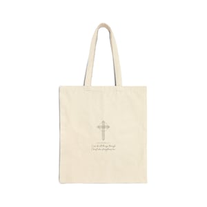 May include: Cream-colored tote bag with a cross design and the text "I can do all things through Christ who strengthens me." The bag has a simple, minimalist design with long handles.