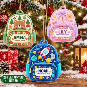 May include: Three backpack-shaped ornaments hanging from gold strings. The green one features a bear, trees, and mushrooms with the text EMMA PRE-K 2026. The pink one shows ballet slippers and a crown with LILY KINDERGARTEN 2026. The blue one displays space motifs with NOAH KINDERGARTEN 2026.