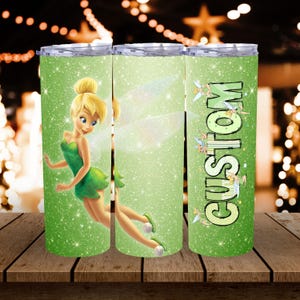 May include: A set of three green glitter tumblers featuring a cartoon fairy design. One tumbler has the word "CUSTOM" in green. The fairy is wearing a green dress and has blonde hair. The tumblers are on a wooden surface.