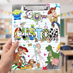 May include: A rectangular clipboard featuring a white lined paper background decorated with various colorful cartoon characters from the Toy Story franchise, including Woody, Buzz Lightyear, and Jessie. The word CUSTOM is printed in large, bold letters.