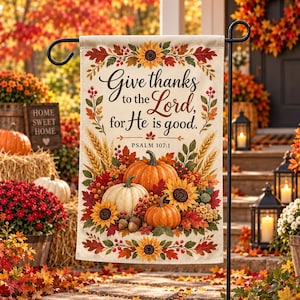 May include: A rectangular garden flag featuring a cream background with a fall-themed border of sunflowers, red leaves, and berries. The text reads, Give thanks to the Lord, for He is good. PSALM 107:1, centered above a cluster of orange and white pumpkins.