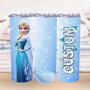May include: A custom tumbler featuring a cartoon image of a princess in a blue dress with a cape. The tumbler has a light blue background with glitter and the word "CUSTOM" in a stylized font.