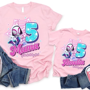 May include: Pink t-shirts with a Spider-Gwen graphic, the number 5, and the names "Mama" and "Amelia". The shirts are paired with blue jeans and white and pink sneakers. A birthday theme.