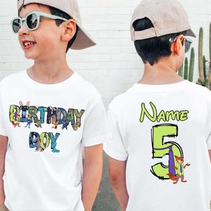 May include: White t-shirt with the words "BIRTHDAY BOY" in colorful letters and cartoon characters. The back of the shirt has the word "Name" and the number "5" with a cartoon fox. A fun birthday shirt.