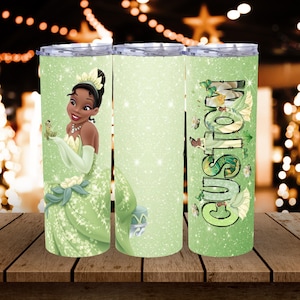 May include: A set of three stainless steel tumblers with lids. The first tumbler features a cartoon image of a princess in a green dress holding a frog. The second tumbler has a glittery green background. The third tumbler has the word "CUSTOM" in green.