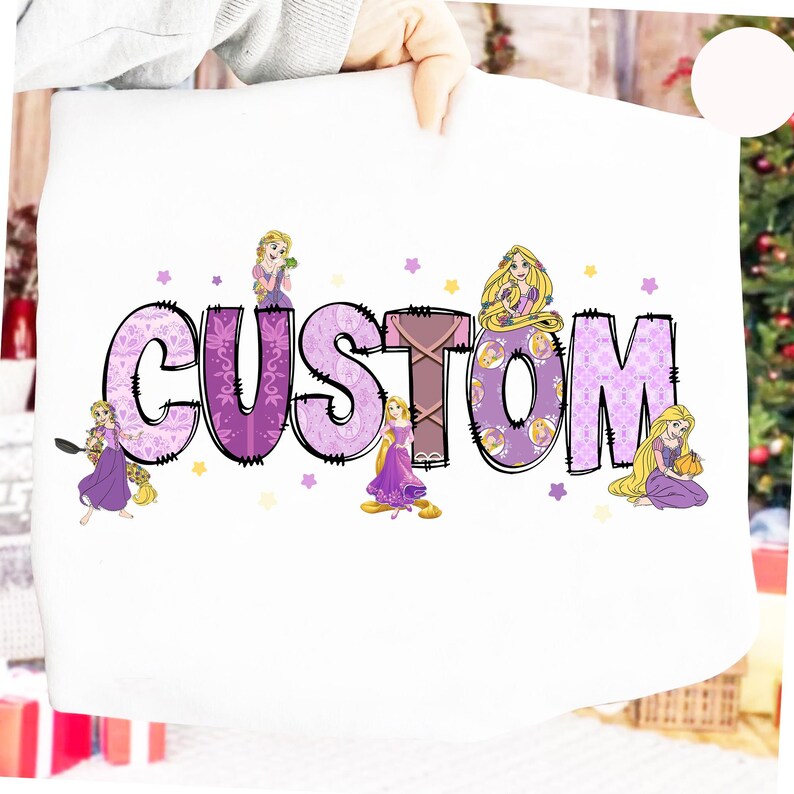 May include: White sweatshirt featuring the word "CUSTOM" in a purple, patterned design with black outlines. The word is decorated with illustrations of a princess. Small stars in yellow and purple surround the word.