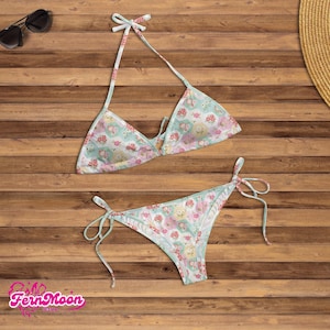 May include: A two-piece bikini set with a floral pattern in pastel colors. The halter top and the bottoms have tie closures. The bikini is light blue with pink and yellow floral designs. Sunglasses and a straw hat are also visible.