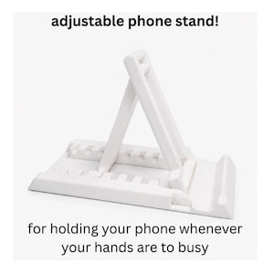 May include: A white adjustable phone stand with a notched base for multiple viewing angles. The text "adjustable phone stand!" appears at the top, and "for holding your phone whenever your hands are to busy" is printed at the bottom of the image.