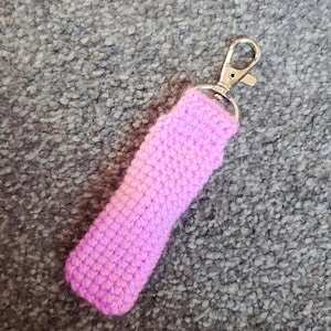 Può includere: Un porta-balsamo per labbra in crochet rosa con un portachiavi in metallo argentato.