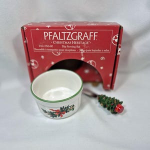 May include: A white Pfaltzgraff Christmas Heritage dip serving set with a green rim and festive holiday design. The set includes a small bowl and a spoon with a Christmas tree handle, presented in a red box.
