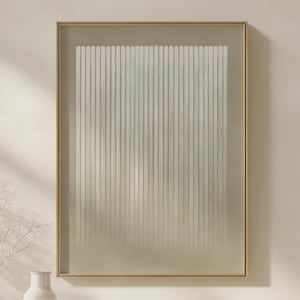 May include: Abstract art print in a gold frame. The artwork features vertical white lines against a soft, gradient background of beige and light green. The framed art is displayed on a neutral-colored wall, creating a minimalist aesthetic.
