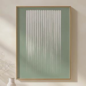 May include: A framed abstract art print featuring vertical white lines against a soft green background. The artwork is encased in a gold-colored frame, creating a minimalist and modern aesthetic. The print's design is simple yet visually appealing.