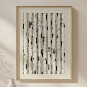 May include: Abstract art print in a gold frame. The artwork features vertical black lines with irregular, textured shapes against a cream background. The framed art is a minimalist design, suitable for home decor.