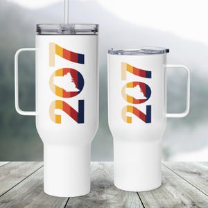 Könnte beinhalten: Zwei weiße Reisebecher mit Griffen und Deckeln. Jeder Becher zeigt die Nummer "207" in einem Retro-Farbschema, mit einer Umrisszeichnung eines Bundesstaates in der Mitte. Ein Becher hat einen Strohhalm.