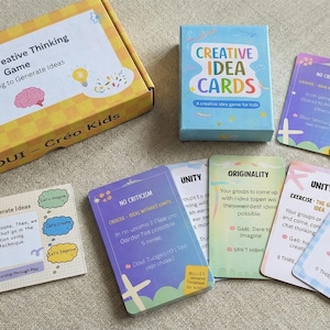 Puede incluir: Un juego de pensamiento creativo para niños, con una caja y una baraja de cartas. La caja amarilla tiene el texto "COUI - Creative Thinking Game" y "Créo Kids". Las cartas son azules y tienen el texto "Creative Idea Cards".