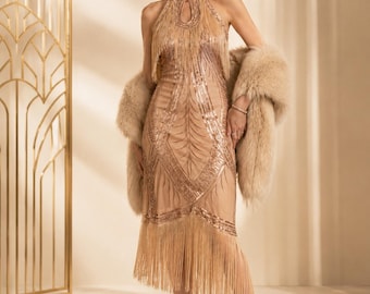 May include: A champagne-colored sleeveless dress featuring a high halter neckline with a keyhole cutout, intricate sequin embroidery in geometric patterns, and long fringe detailing along the bodice and hem, paired with a beige faux fur stole.