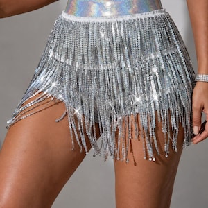 May include: A pair of silver shorts featuring a high-waisted band with a holographic finish. The shorts are covered in multiple layers of long, shimmering silver sequin fringe that hangs down from the waist, creating a dynamic, reflective effect.