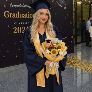 Może przedstawiać: Absolwentka w granatowej czapce i todze ze złotą szarfą, trzymająca bukiet słonecznik&oacute;w i misia. Tło przedstawia baner z napisem "Congratulations Graduation CLASS OF 2024."