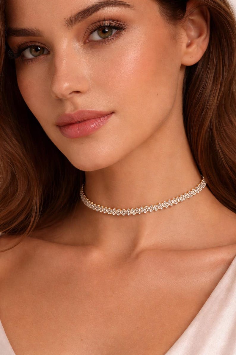 May include: A close-up of a woman wearing a delicate, sparkling choker necklace. The necklace is made of small, round, clear crystals set closely together, creating a continuous band of shimmer. The necklace sits around the base of the neck.