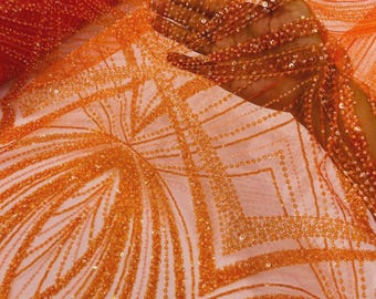 May include: A vibrant orange mesh fabric featuring intricate embroidery and dense sequin embellishments. The design consists of geometric patterns, including sharp angles and radiating lines, created with rows of small, reflective orange sequins.