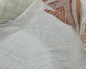 May include: A sheer white fabric featuring intricate embroidery with white beads and sequins arranged in a geometric pattern of lines and diamonds. The material is semi-transparent and displays a repeating decorative design across the surface.