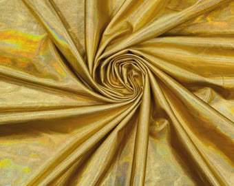 May include: A piece of metallic gold fabric with a holographic finish, featuring a swirling, gathered texture that creates deep folds and highlights. The material displays a reflective, shimmering surface with subtle rainbow color shifts.