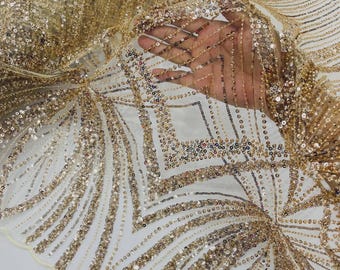 May include: A sheer, light-colored fabric featuring an intricate, geometric pattern of gold sequins and metallic thread embroidery. The design consists of repeating diamond shapes and radiating lines, creating a dense, shimmering texture throughout.