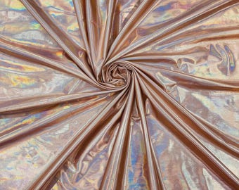 May include: A rose gold fabric with a high-gloss, metallic finish that displays a holographic, iridescent sheen. The material is gathered at the center, creating radiating folds and pleats that emphasize the reflective, light-catching surface.
