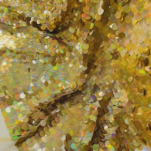 May include: Close-up of a shimmering gold sequin fabric. The sequins are round and overlapping, creating a textured surface. The fabric reflects light, displaying iridescent colors. Ideal for crafting, fashion, or decorative projects.