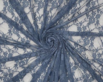 May include: A dusty blue lace fabric featuring a delicate floral pattern. The material is gathered in a central spiral, showcasing the intricate, semi-sheer mesh construction and the repeating botanical motifs woven throughout the textile surface.