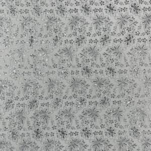 May include: White lace fabric with a floral pattern. The design features embroidered flowers and leaves with silver sequins. The edge of the fabric has a scalloped trim. This fabric is suitable for bridal wear, dresses, or other craft projects.
