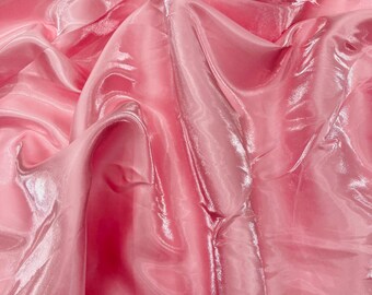 May include: Close-up of a pink, shiny fabric with a flowing, rippled texture. The fabric has a glossy sheen, reflecting light and creating highlights and shadows. The material appears to be lightweight and delicate, with a soft, flowing drape.
