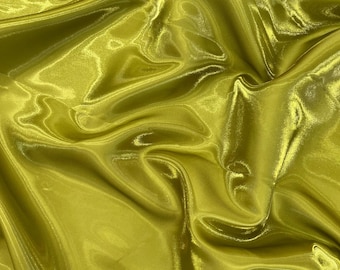 May include: Close-up of a shimmering, golden-yellow fabric with a satin-like sheen. The material is heavily draped, creating soft folds and highlights. The fabric's surface reflects light, giving it a luxurious appearance. Ideal for apparel or decorative projects.