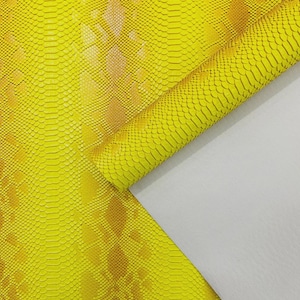 May include: Vibrant yellow faux snakeskin material with a textured pattern and a rolled edge. The material has a gold and yellow gradient, and the backing is white.