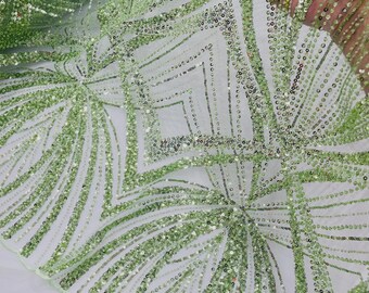 May include: A sheer lime green fabric featuring an intricate pattern of embroidered lines and shimmering sequins. The design consists of repeating geometric diamond shapes and radiating fan-like motifs, creating a textured and reflective surface.
