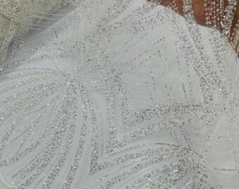 May include: A white sheer fabric featuring intricate silver sequin embroidery in a geometric pattern. The design includes repeating diamond shapes and fan-like motifs with dense beadwork, creating a highly reflective and textured surface.