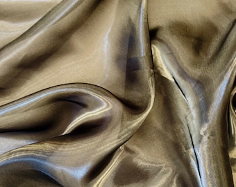 May include: Close-up of a shimmering, flowing fabric in a muted olive-green color. The material has a silky, reflective quality, with soft folds and highlights that create a sense of depth and movement. Ideal for apparel or home decor.
