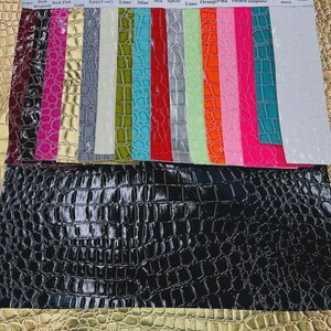 May include: A collection of colorful faux leather swatches, including black, gold, and various shades of pink, green, and blue. The swatches have a crocodile skin texture. The top row has color names printed on it.