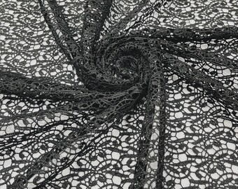 May include: A black lace fabric featuring a continuous, intricate floral pattern with openwork detailing. The material is gathered into a central spiral, showcasing the delicate, interconnected mesh structure and the fine, repeating thread design.