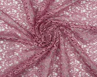 May include: A dusty rose pink lace fabric featuring an intricate, repeating floral and vine pattern. The material is gathered in the center, creating a swirling, textured effect that highlights the delicate, openwork mesh construction.