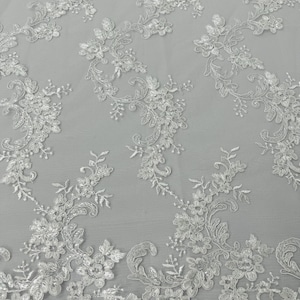 Peut inclure: Tissu de dentelle florale blanche avec des fleurs et des feuilles brodées. La dentelle délicate présente un bord festonné et se détache sur un fond gris clair. Ce tissu élégant convient aux robes de mariée, aux robes ou aux projets décoratifs.