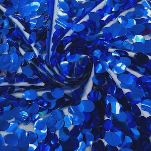 May include: A close-up shot of a fabric covered in bright blue sequins. The circular sequins are densely packed, creating a shimmering effect. The fabric is draped, with folds and shadows adding depth. The overall effect is one of luxury and glamour.