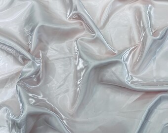 May include: A close-up shot of a shimmering, light-colored fabric with a glossy sheen. The fabric has soft folds and a subtle gradient of pink and silver hues, creating a flowing, elegant appearance. The material appears to be lightweight and delicate.