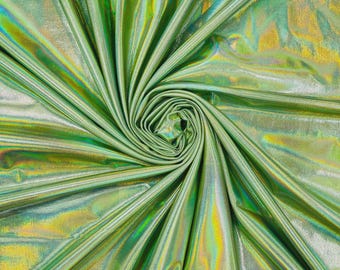May include: A piece of fabric with a metallic, holographic finish that shifts between shades of lime green, yellow, and light blue. The material is gathered into a central spiral, creating deep, radiating folds that highlight the reflective surface.