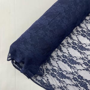 Könnte beinhalten: Eine Rolle marineblauen Spitzenstoffs. Die Spitze hat ein Blumenmuster mit detaillierten Designs. Der Stoff ist teilweise abgerollt und zeigt die filigrane offene Arbeit der Spitze. Der Hintergrund ist eine schlichte weiße Oberfläche.