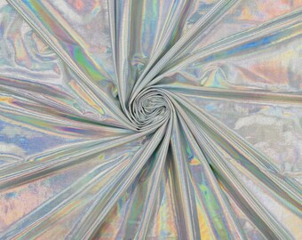 May include: A silver fabric with a high-gloss, holographic finish that reflects a spectrum of iridescent colors. The material is gathered into a central spiral, creating radiating folds and pleats that emphasize the metallic, reflective surface.